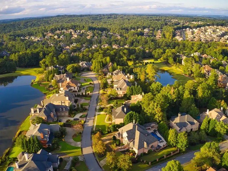 Aerial view of a suburban neighborhood with houses, trees, and lakes.