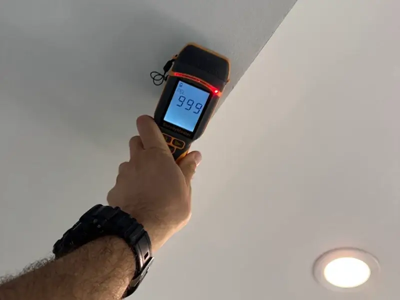 Hand holding a laser distance meter up to the ceiling.